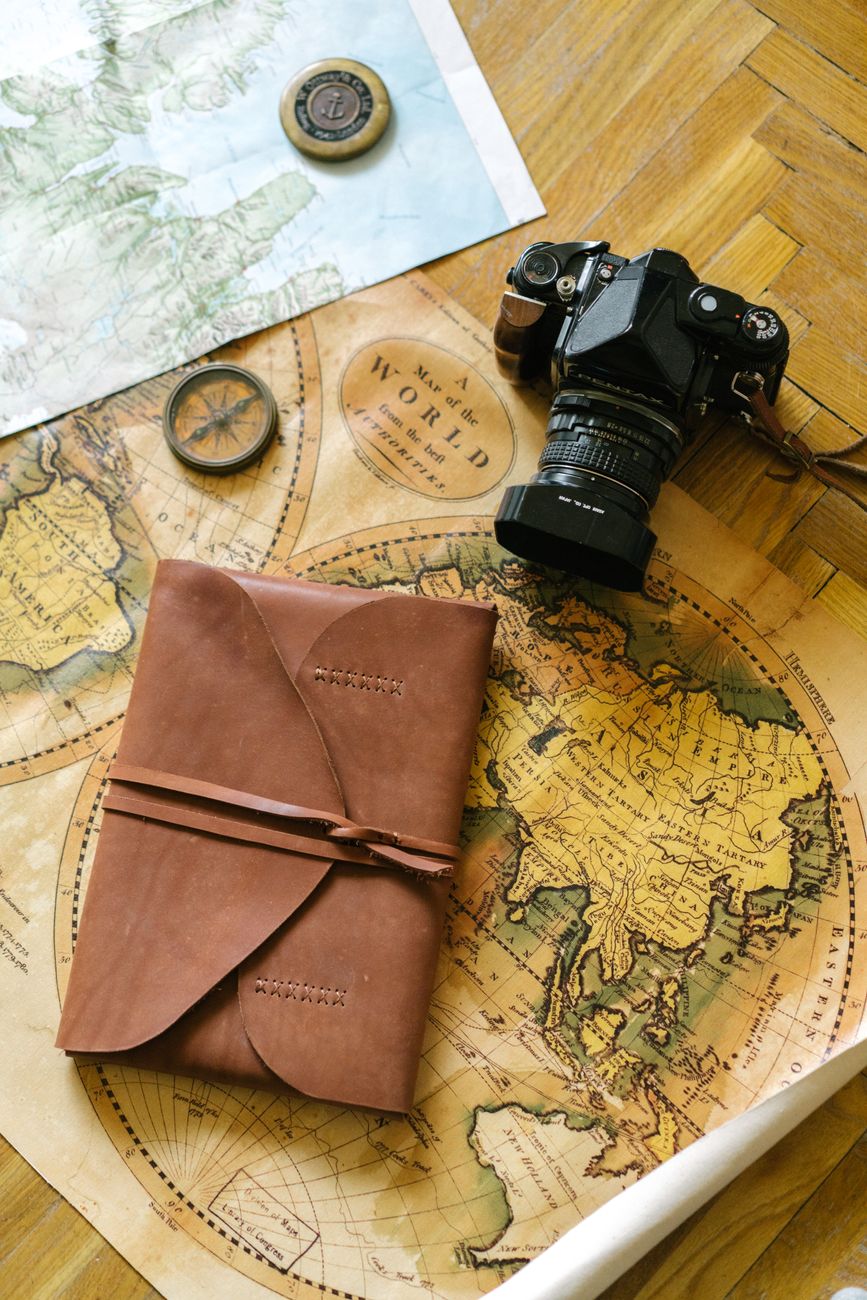 Travel designer studying detailed cartographic maps with leather journal